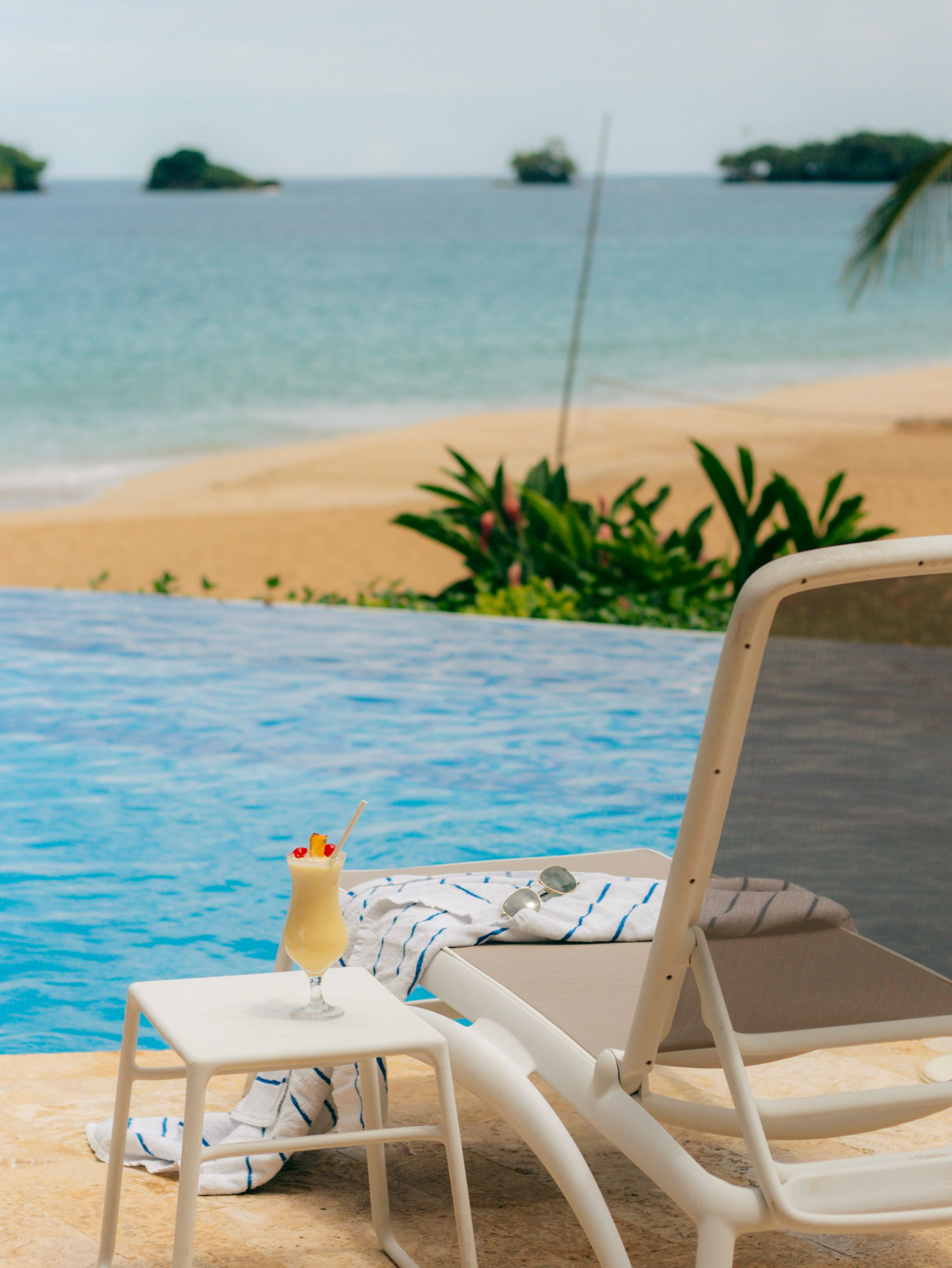 Beachside lounge chair beside an infinity pool with a tropical beach and sea in the background