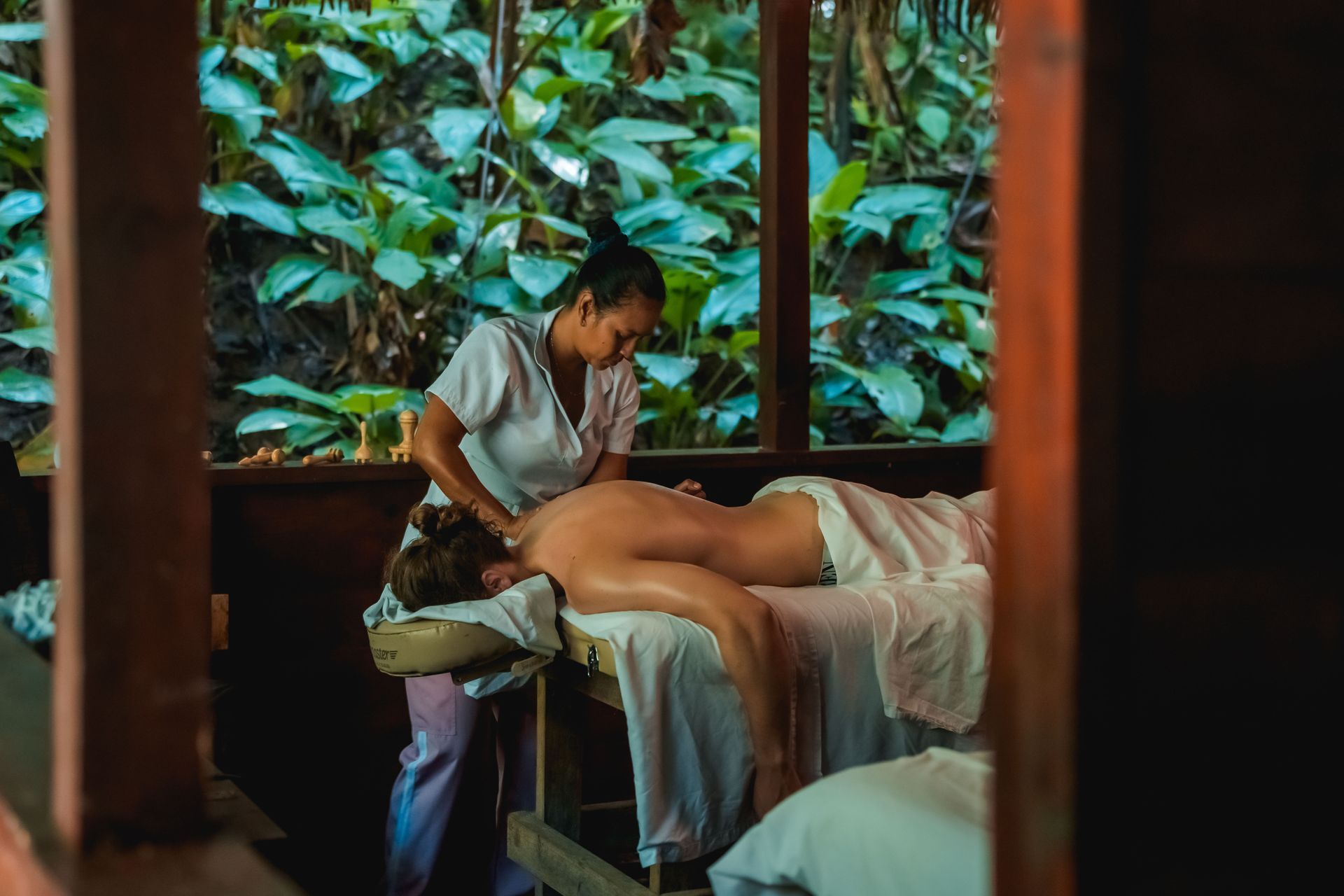 Massage therapist working on a client at a spa with lush green plants outside the window