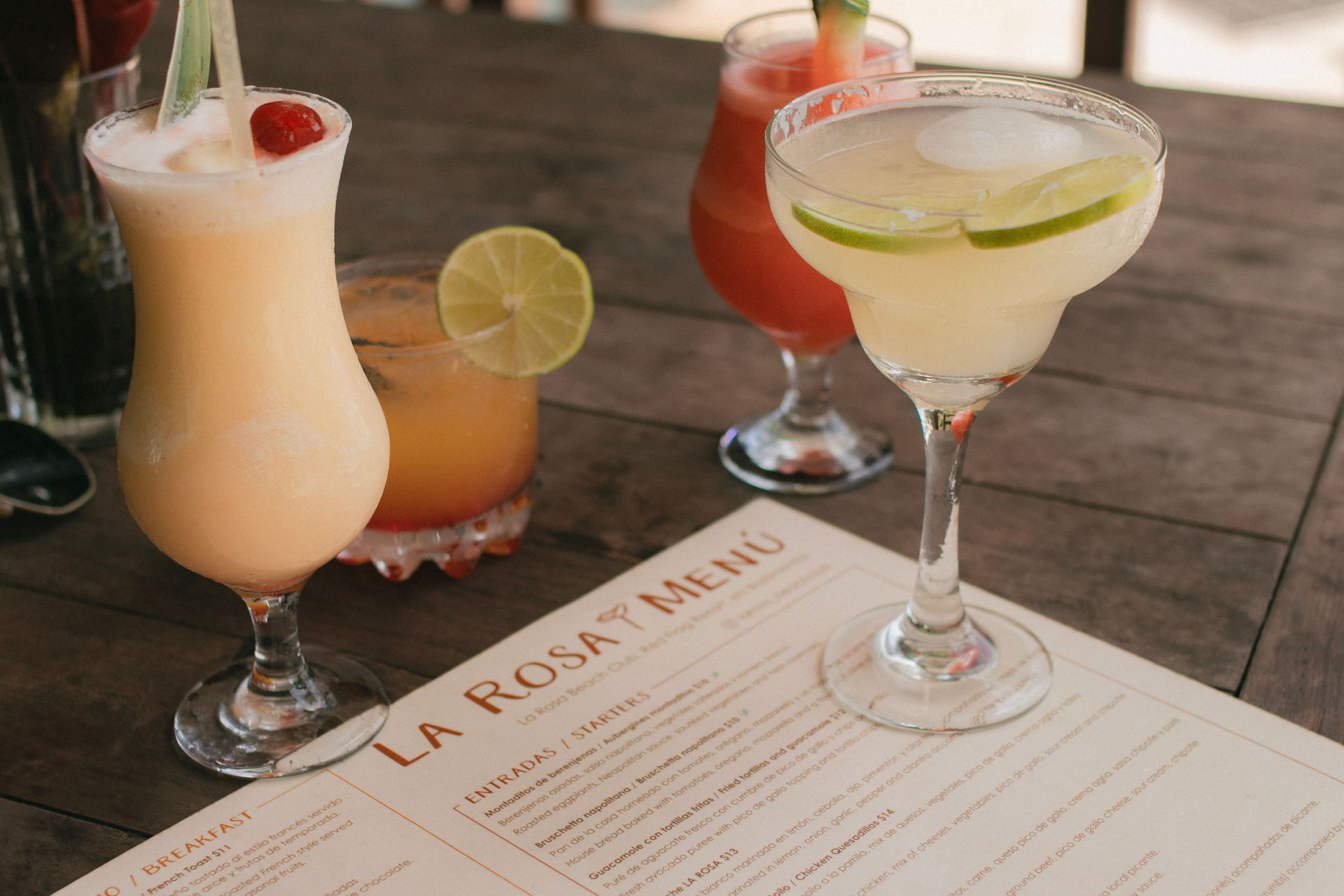 Three colorful cocktails on a table beside a menu titled “La Rosa Menu”