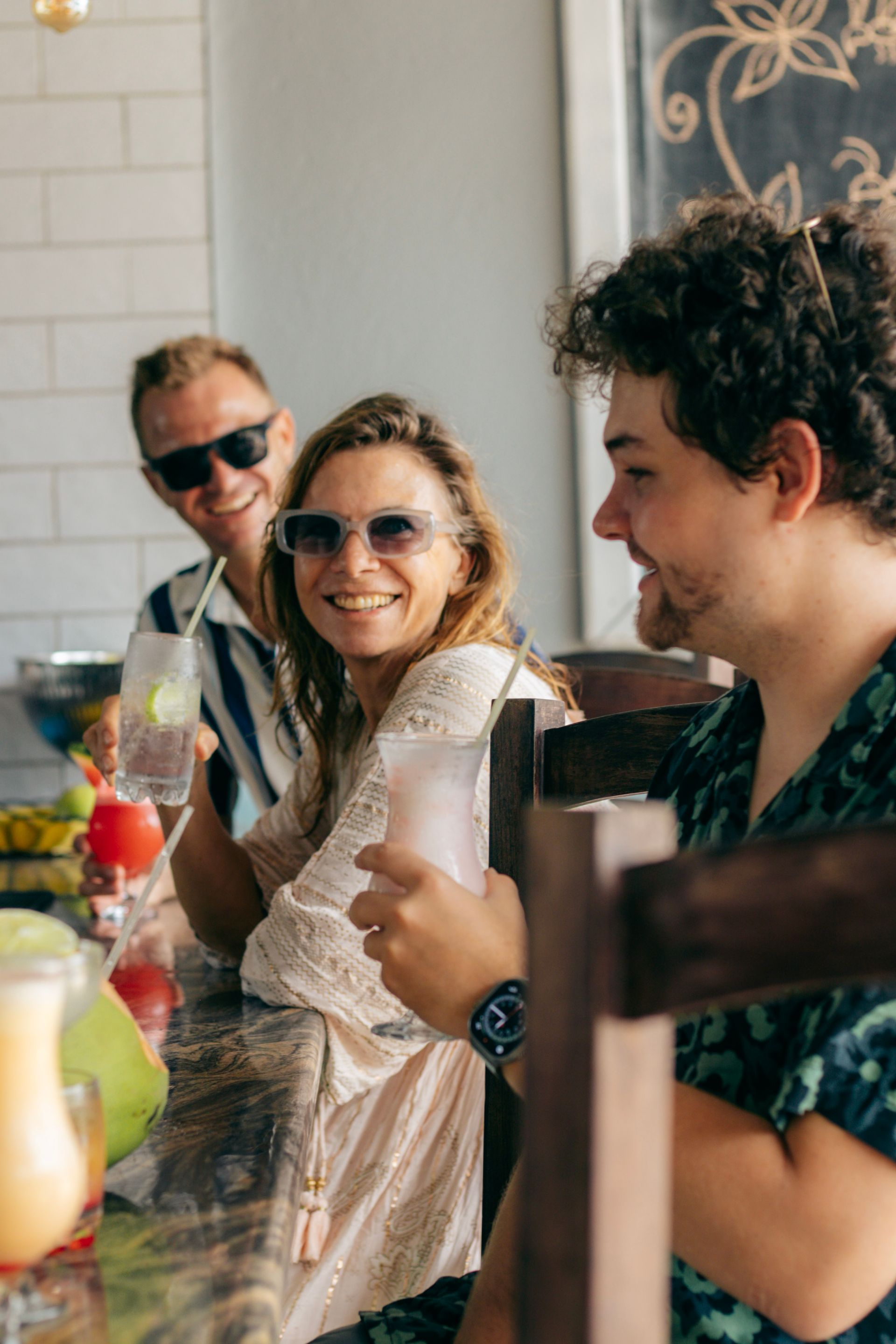 Three friends smiling and chatting at a table, with drinks in a bright café setting