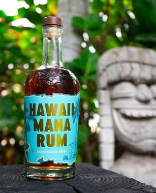 Hawaii Mana Rum bottle on a wooden surface, featuring vibrant turquoise label with bold text, surrounded by lush greenery, representing the essence of Haleiwa Distilling Company and the spirit of Hawaii.