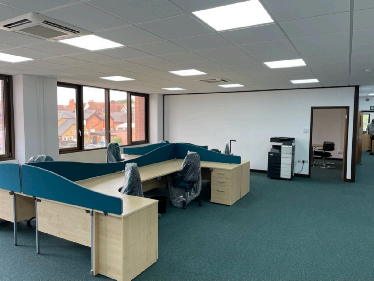 Newly fitted office workspace with desks, partition screens, LED ceiling lights, and covered chairs.