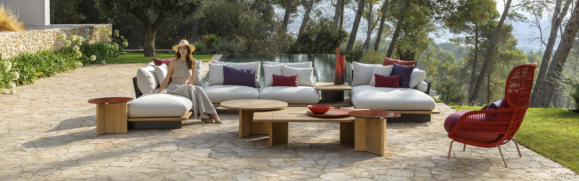 Woman sits on outdoor white sectional sofa with coffee tables, surrounded by trees.