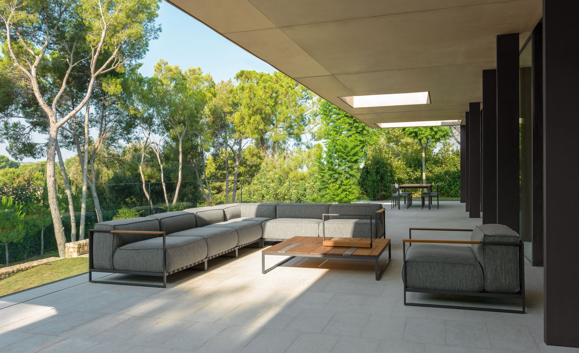 Modern outdoor patio with gray sectional, wooden coffee table, and greenery.