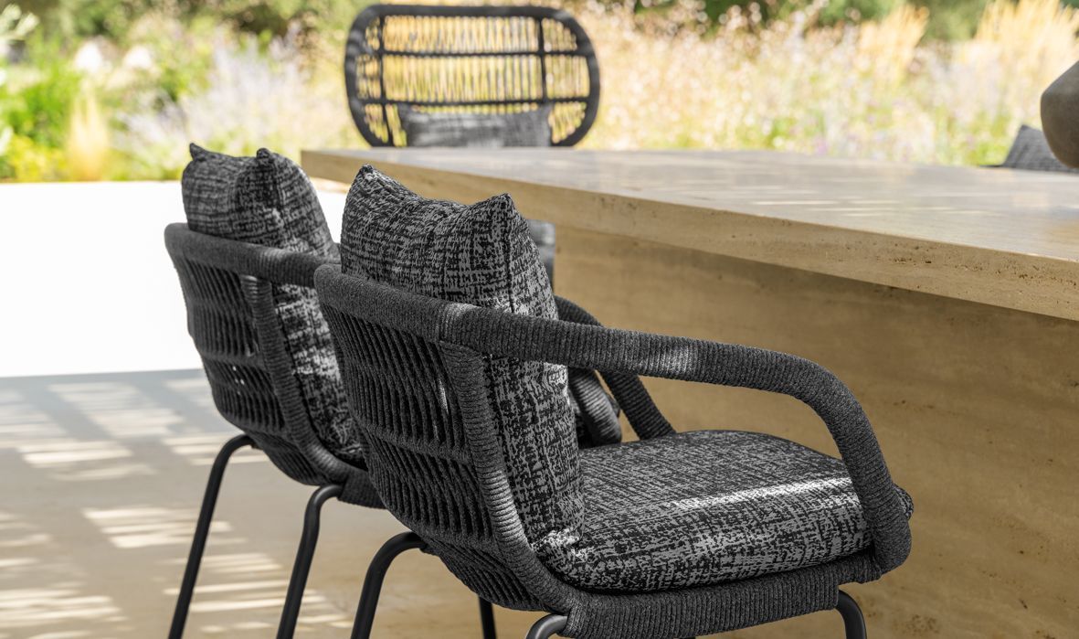 Two black woven outdoor chairs with cushions, on a patio, with a third chair in the background.