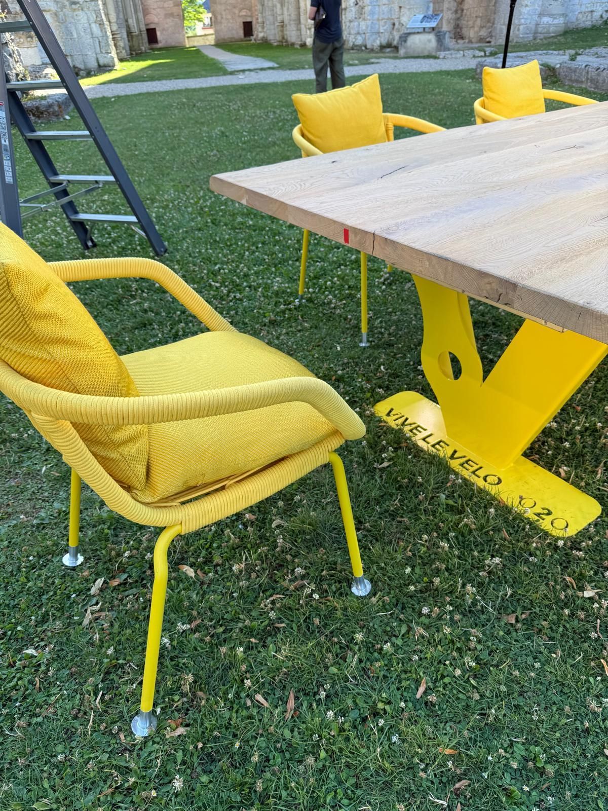 Yellow table and chairs on grass. Wooden table on yellow base. Chairs have yellow cushions.