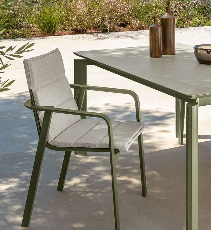 Green metal outdoor chair with cushioned seat and back, beside a matching table.