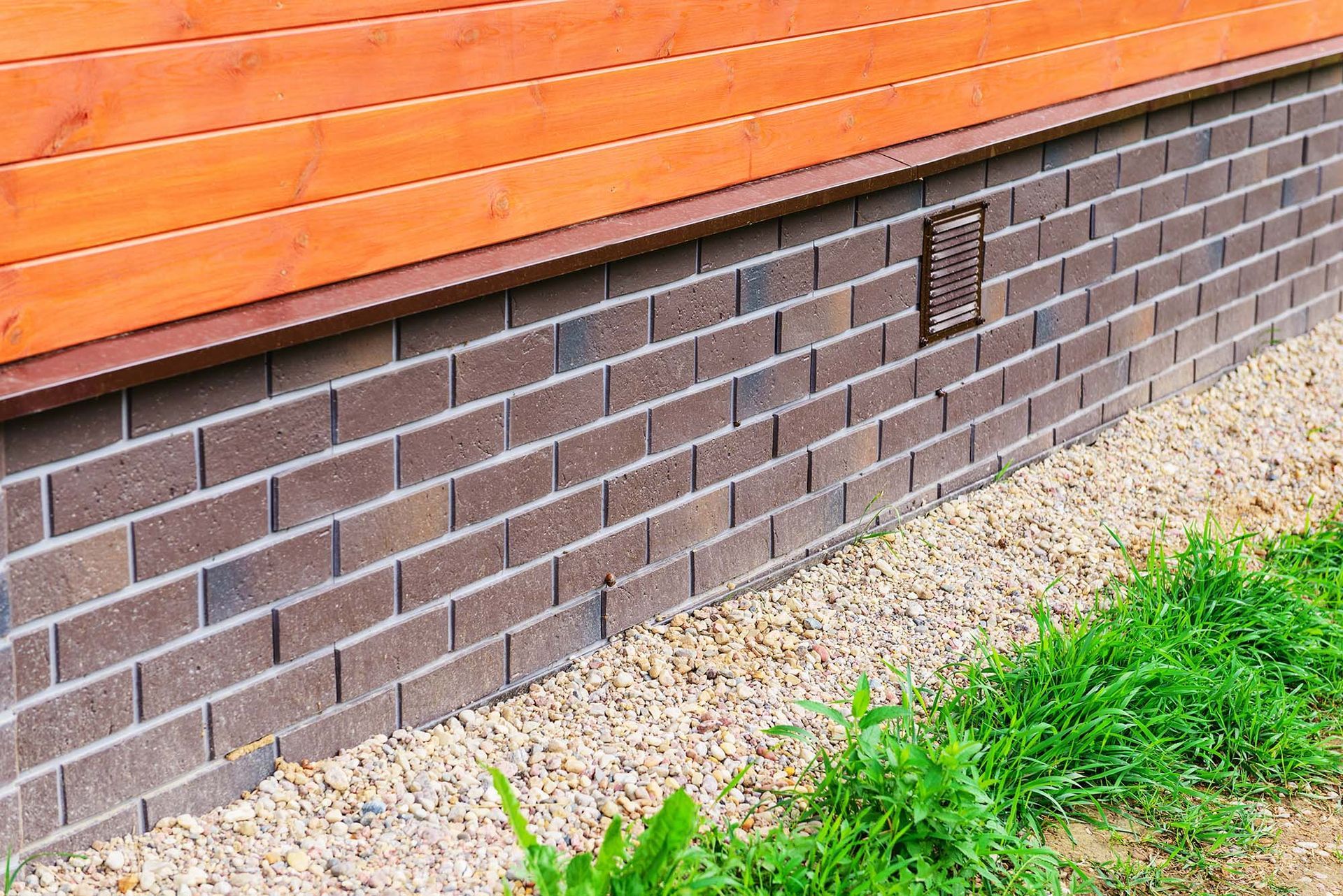Brick house foundation with orange siding, gravel border, and green grass along the side.