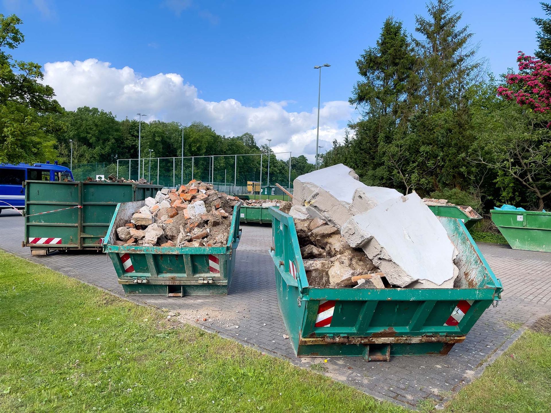 Green dumpsters filled with construction rubble and debris in an outdoor lot on a sunny day