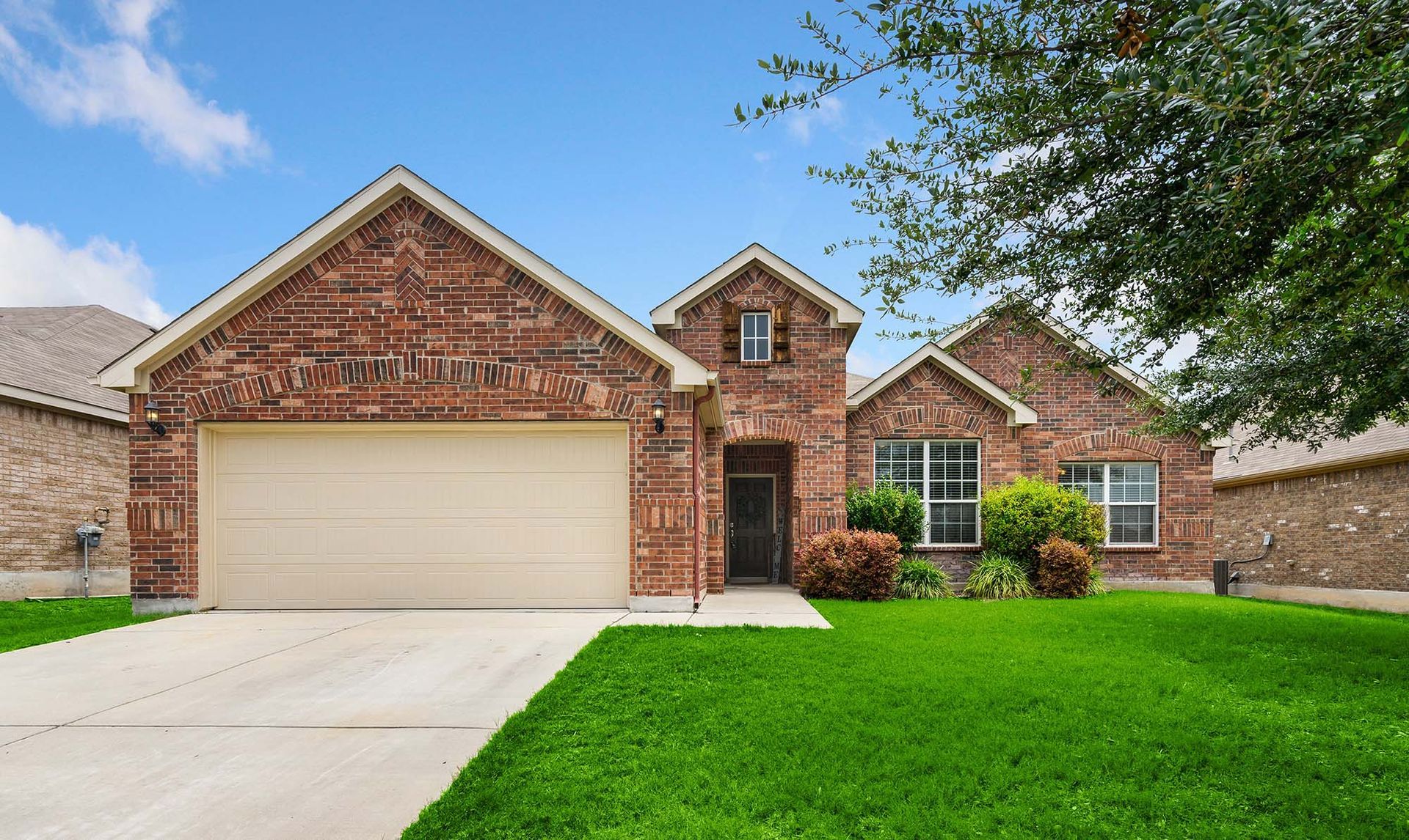 Single-story brick house with beige garage, driveway, and bright green lawn under a blue sky