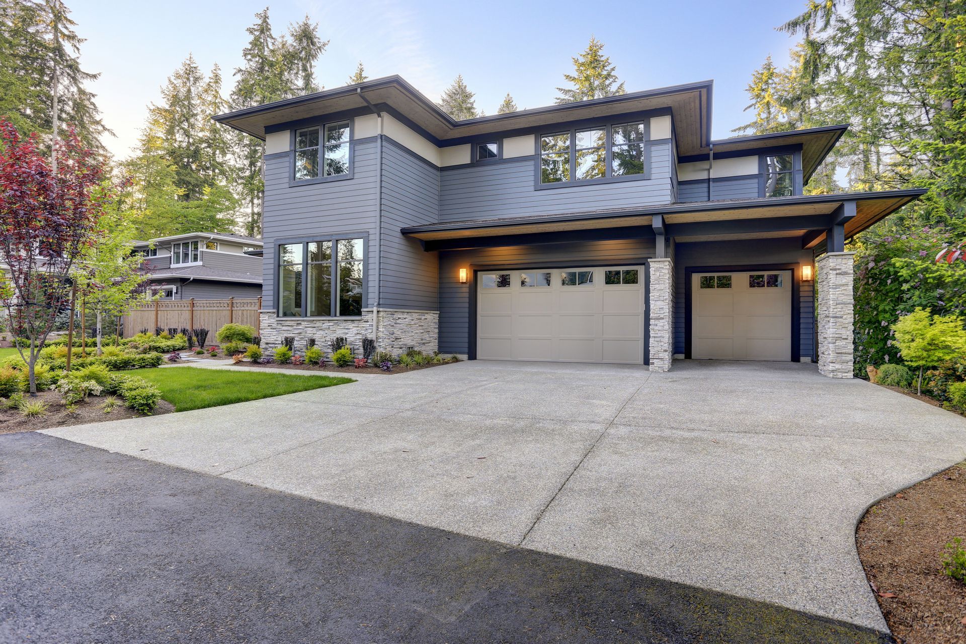 New construction home exterior with contemporary house plan features gray wood siding, stone columns and two garage spaces.