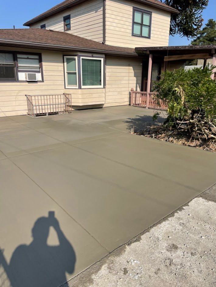 A shadow of a person is cast on a concrete driveway in front of a house.