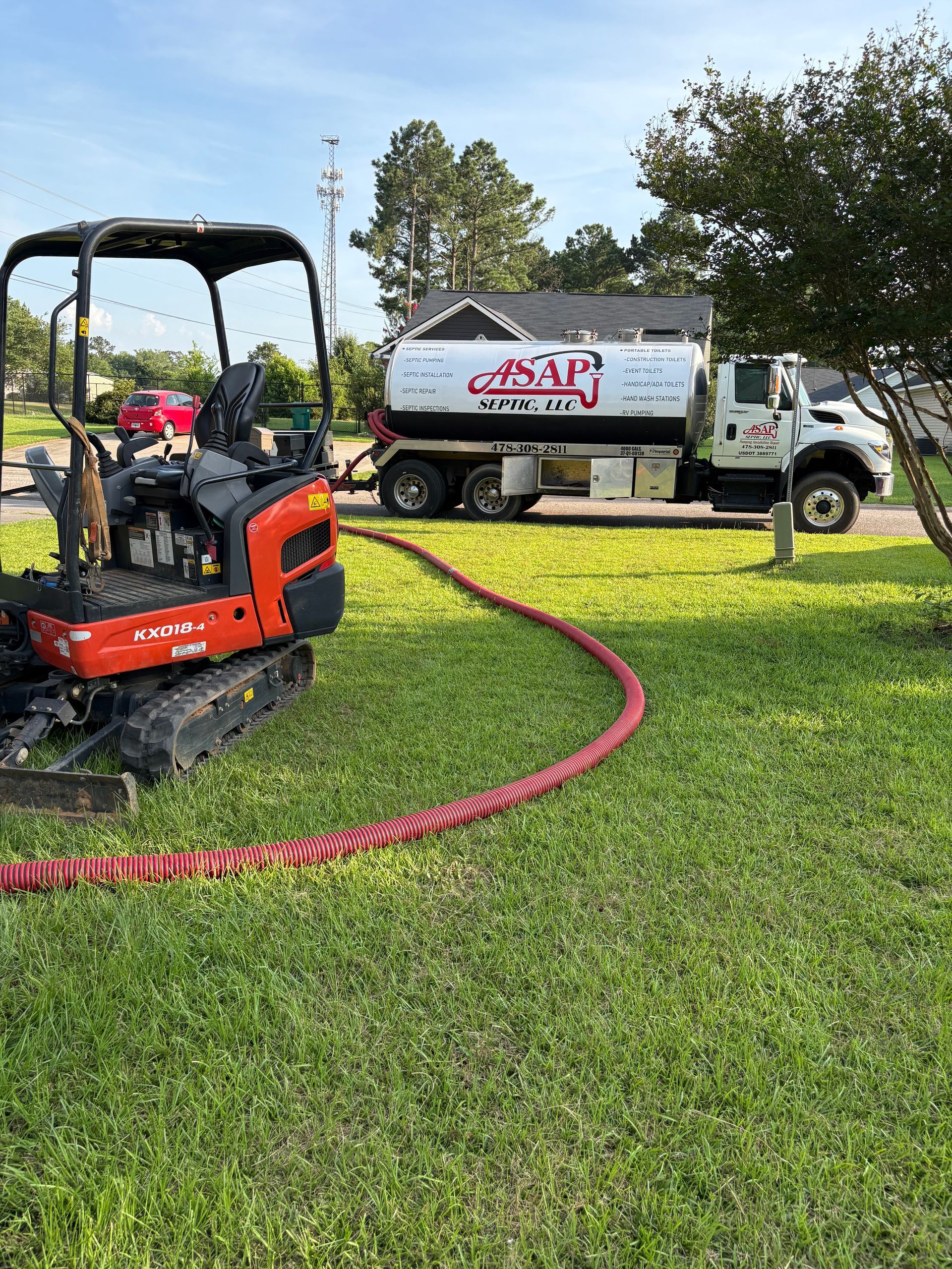 Orange mini excavator on grass beside a white utility truck with a red hose in a yard