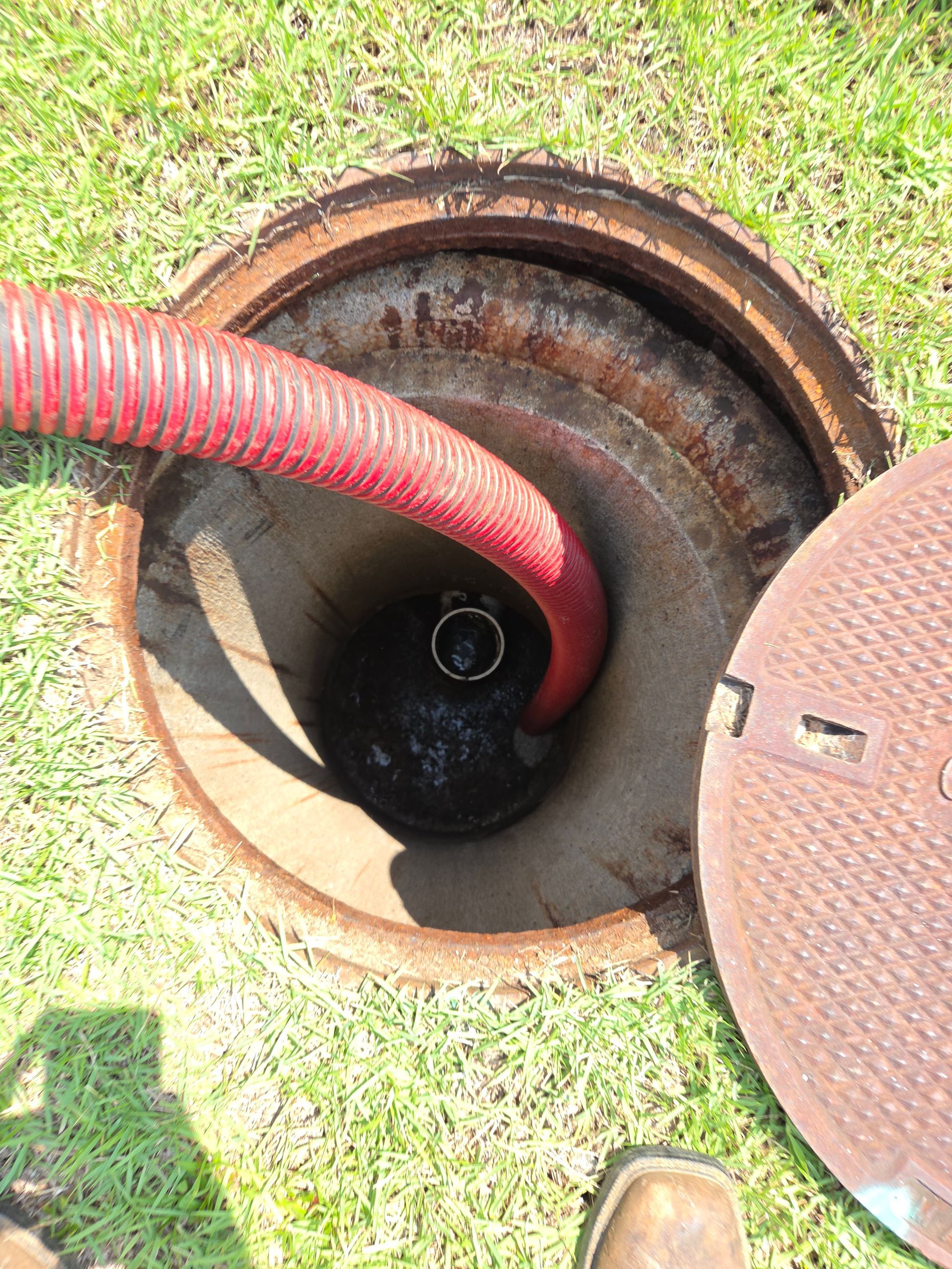 Open sewer manhole with rusty cover. A person stands nearby. Cables are inside.