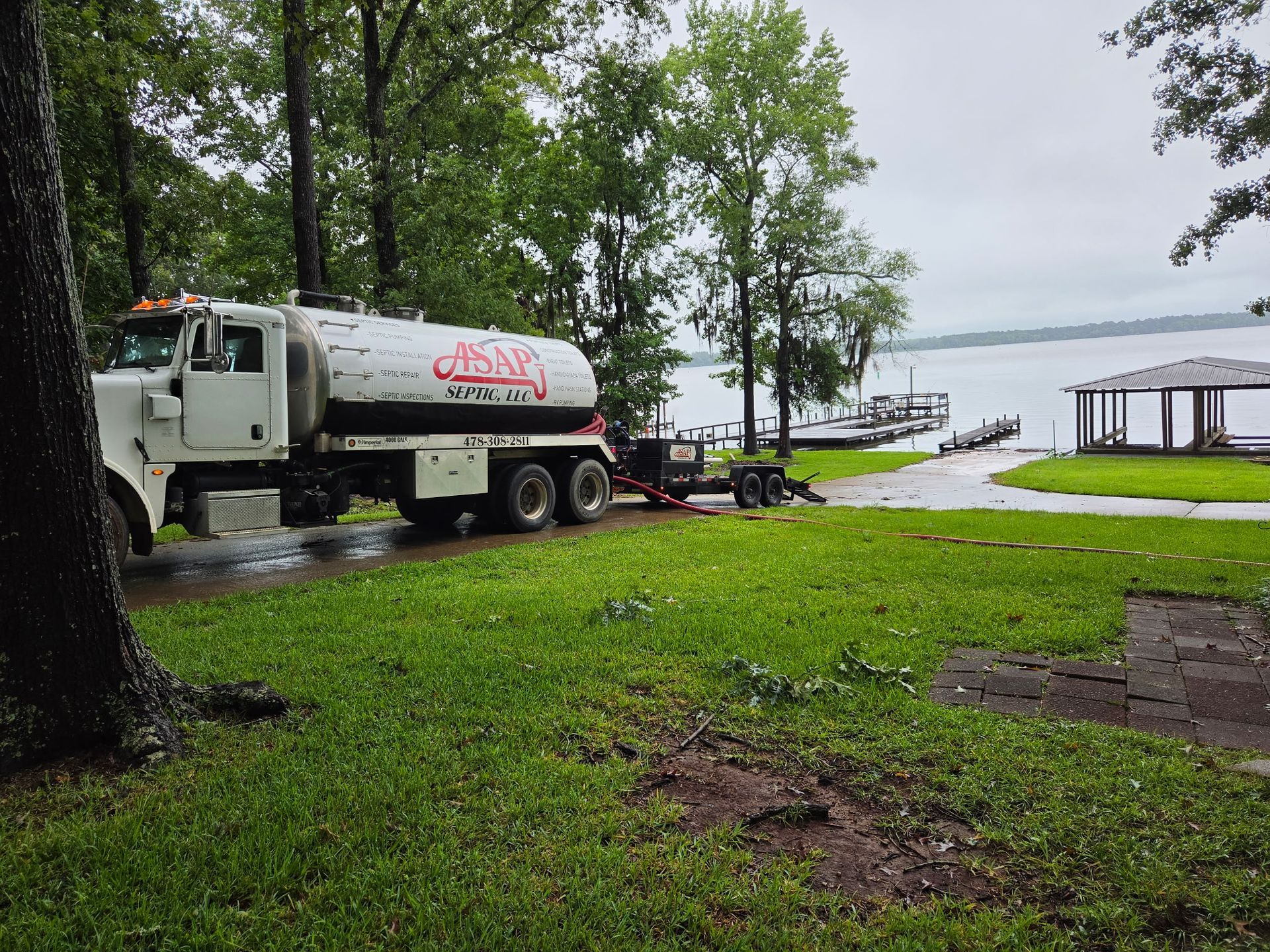 Person in boots and gloves pumping septic tank, lid and hole in grass.