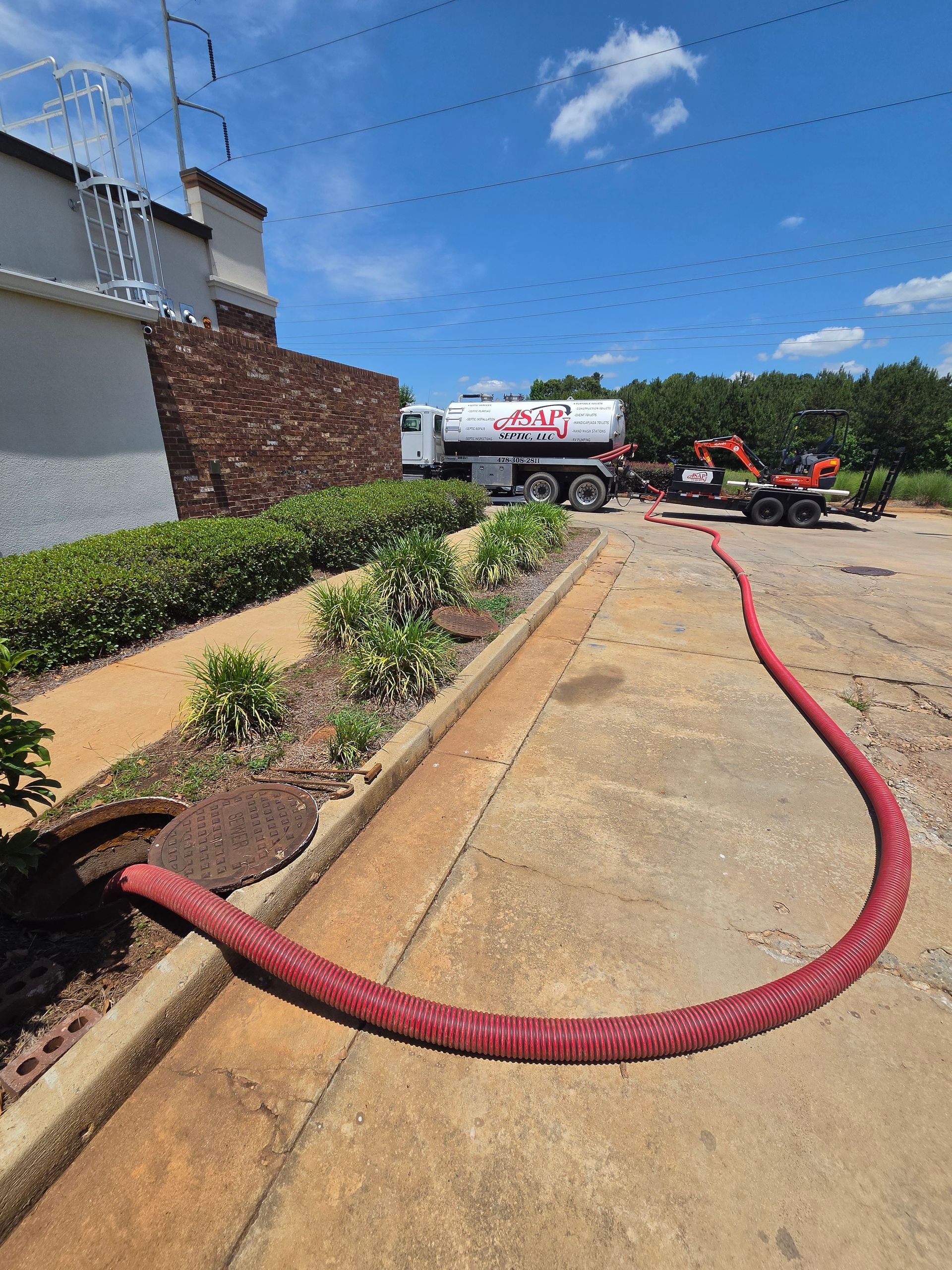 Person in gloves holding a large, red corrugated hose near a brick building.