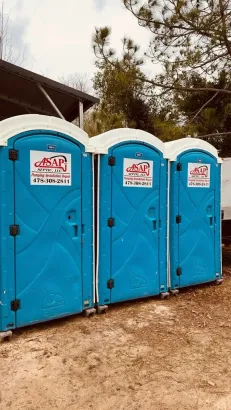 Three blue portable toilets with white tops, lined up outdoors.