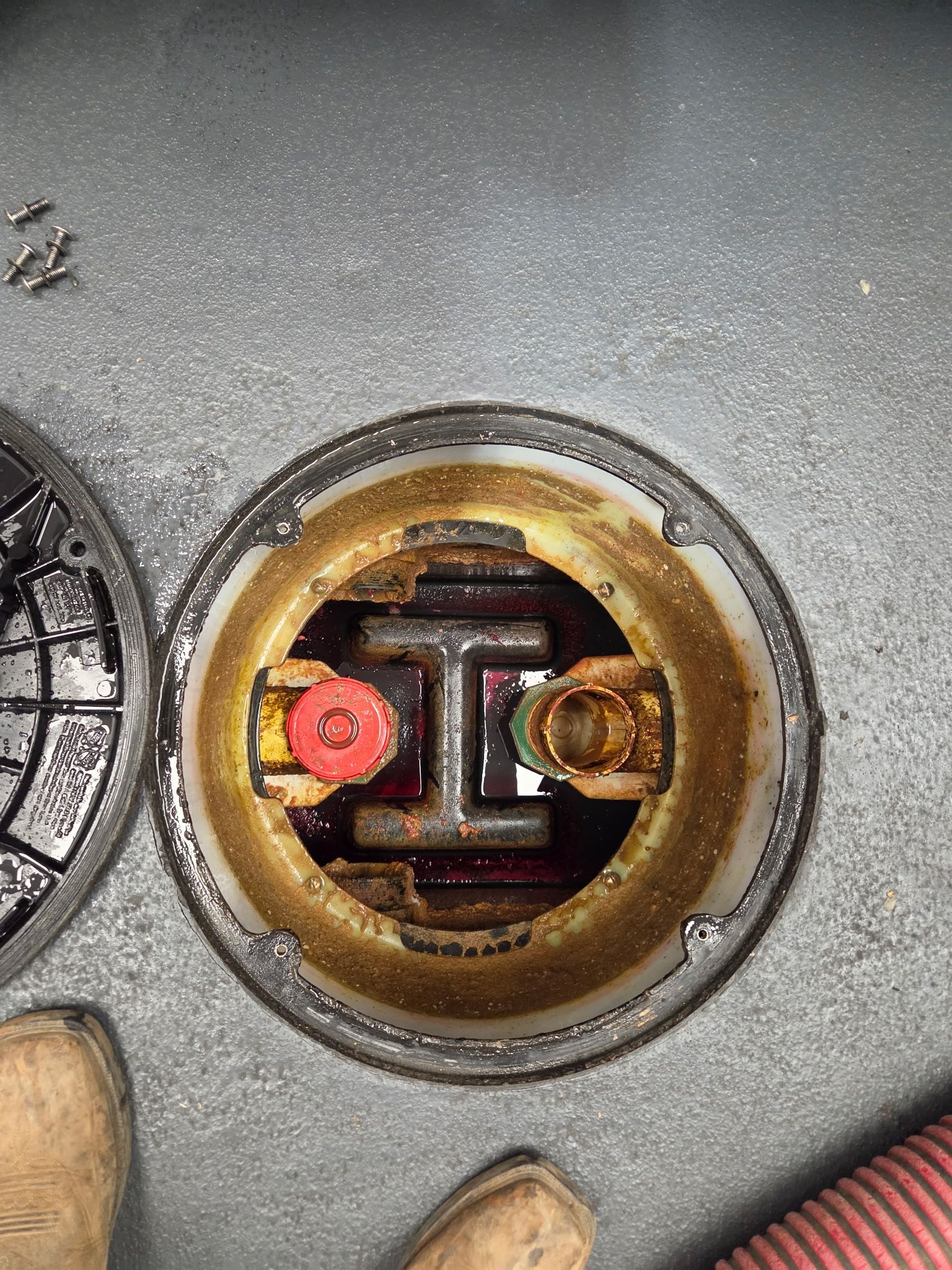 Person pumping sewage from an open manhole. The manhole is square-shaped, surrounded by concrete.
