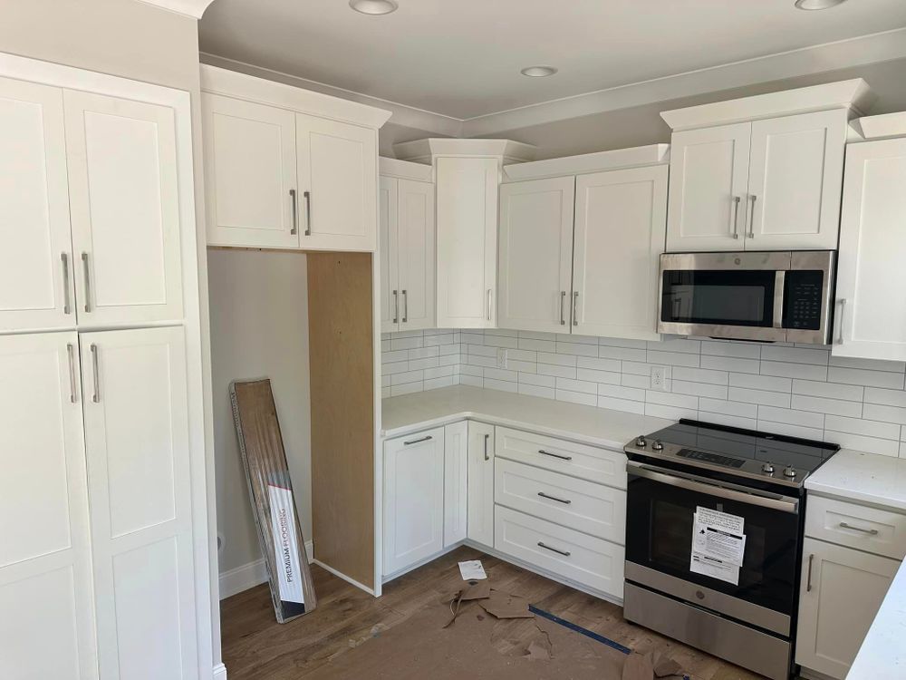 A kitchen with white cabinets , a stove , a microwave and a refrigerator.