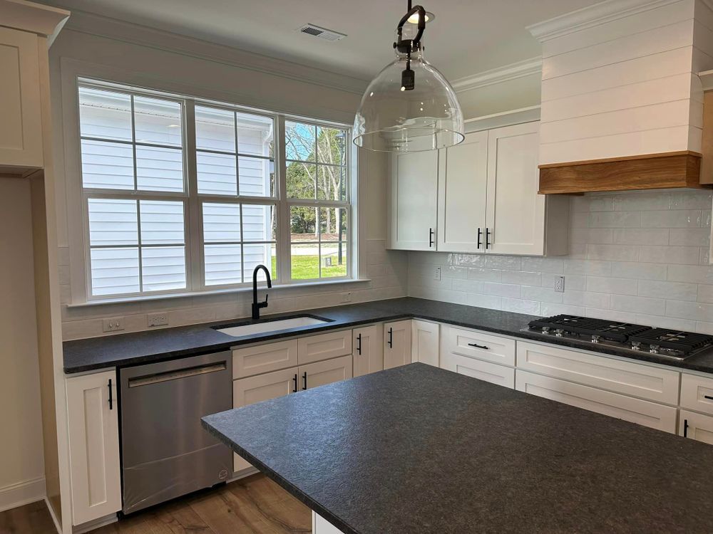 A kitchen with white cabinets , black counter tops , stainless steel appliances and a large island.