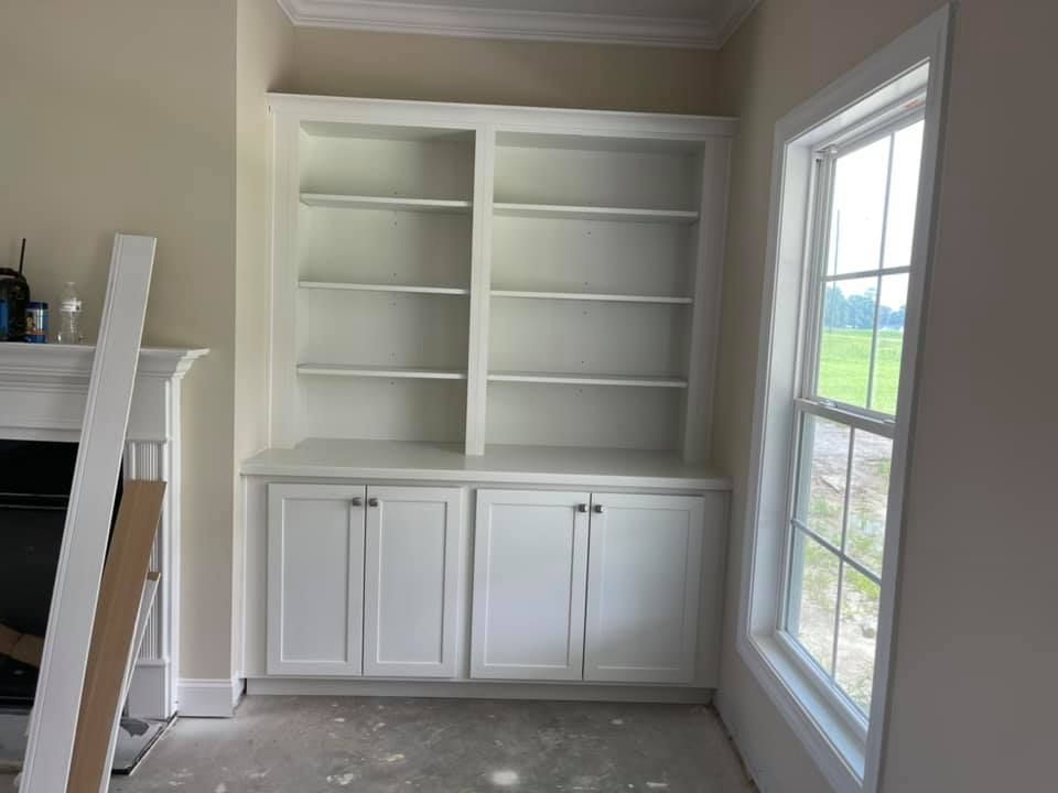 A living room with white cabinets , shelves , a fireplace and a window.
