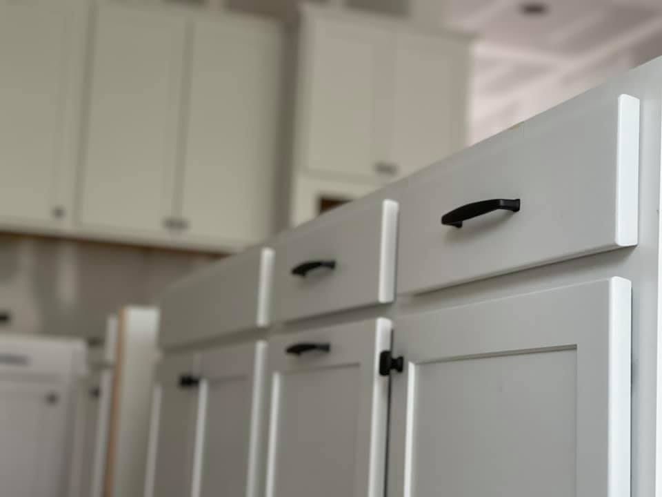 A row of white cabinets with black handles in a kitchen.