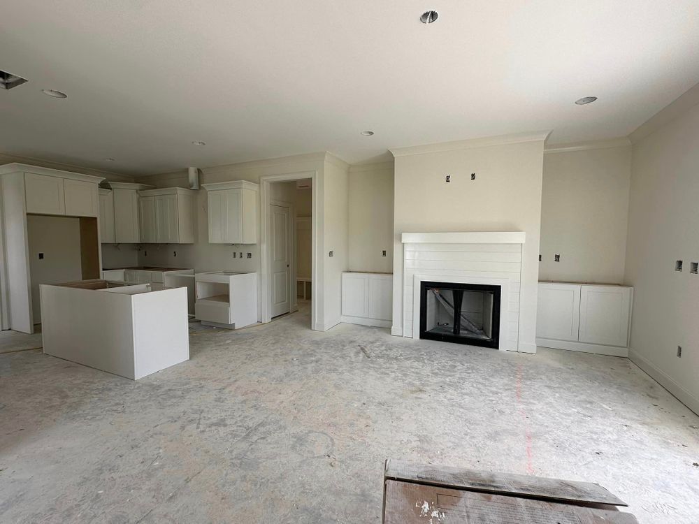 An empty living room with a fireplace and a kitchen in the background.