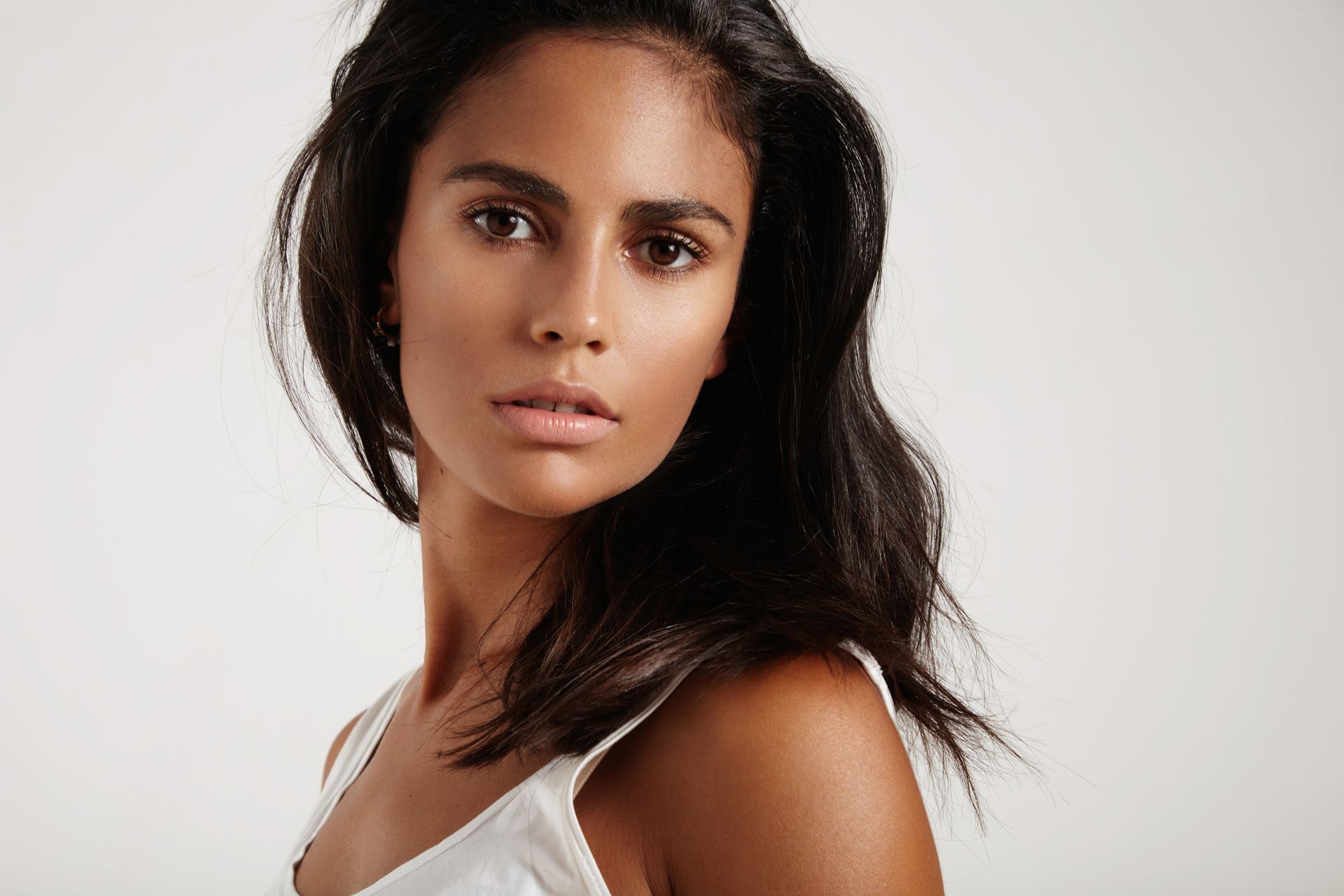 The woman is wearing a white tank top and looking at the camera.