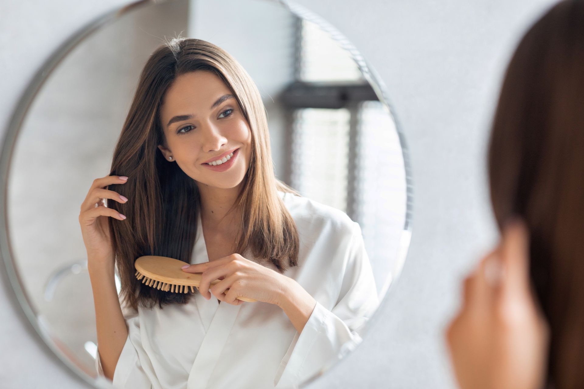 A woman is brushing her hair in front of a mirror.
