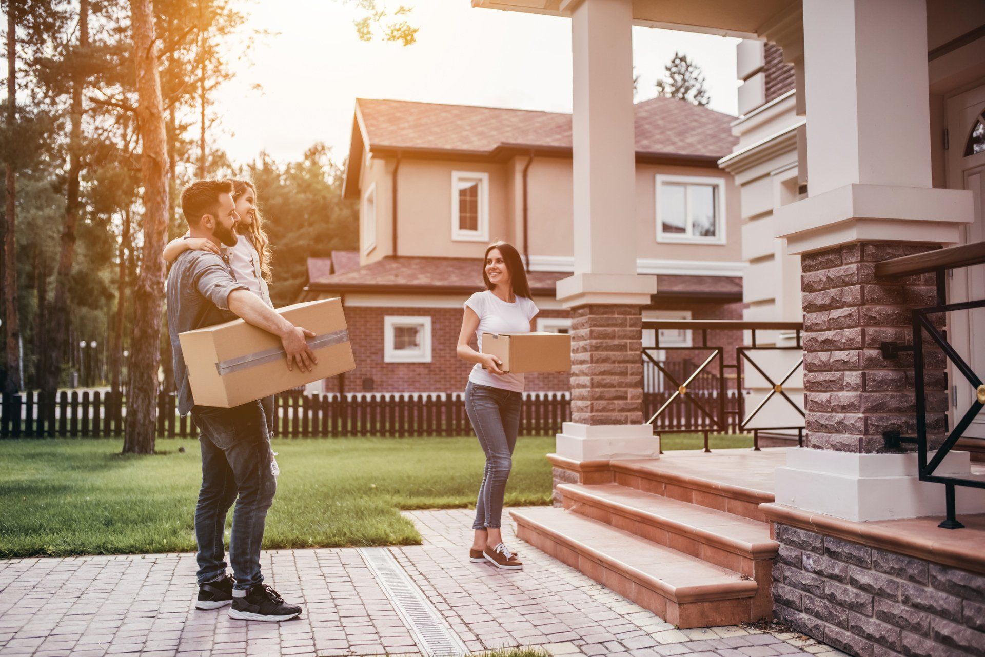 A man and a woman are standing in front of a house holding boxes.