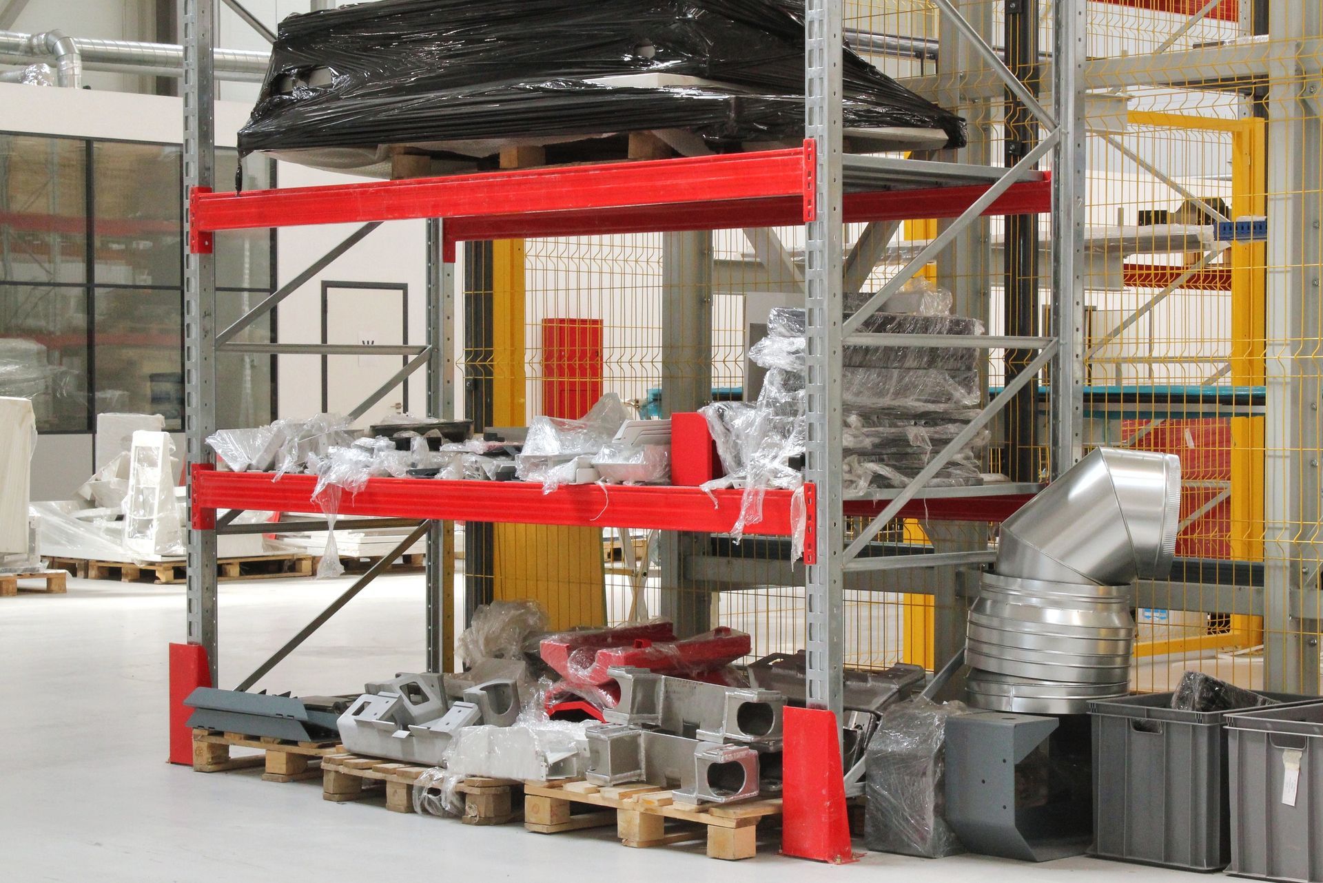 Warehouse shelves with wrapped metal parts, tools, and pallets in an industrial storage area