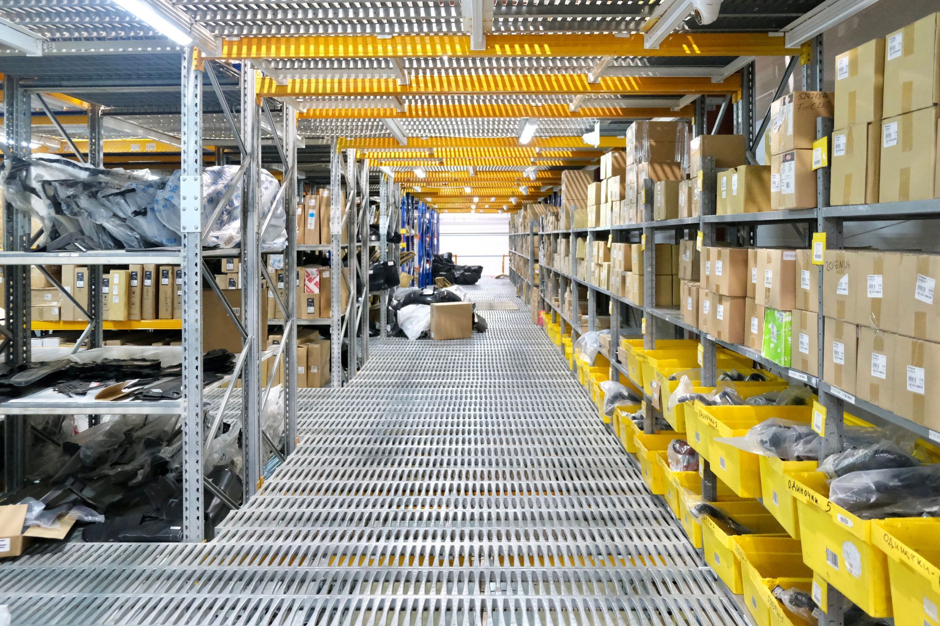 Warehouse aisle with metal shelving, yellow bins, and boxes under bright industrial lighting