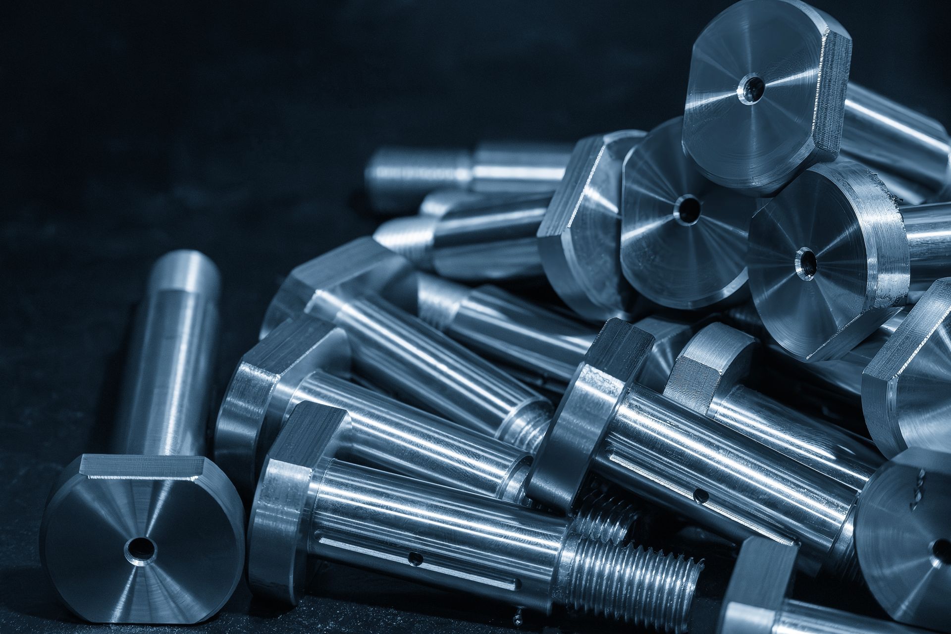 Pile of shiny metal bolts and machined cylindrical parts on a dark surface