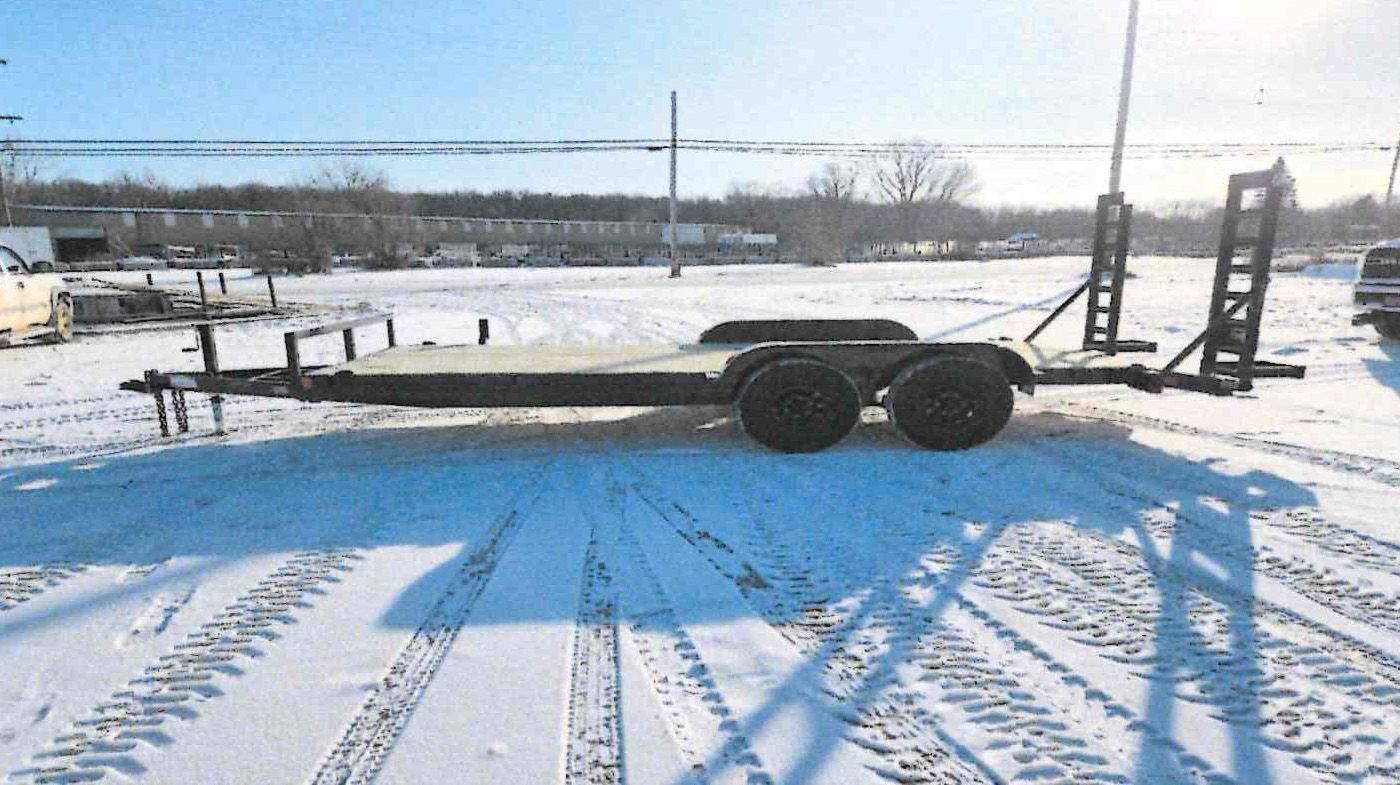 Flatbed trailer parked on a snowy roadside under a bright winter sky.