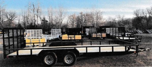 Black utility trailer with metal side rails parked outdoors in a snowy lot.