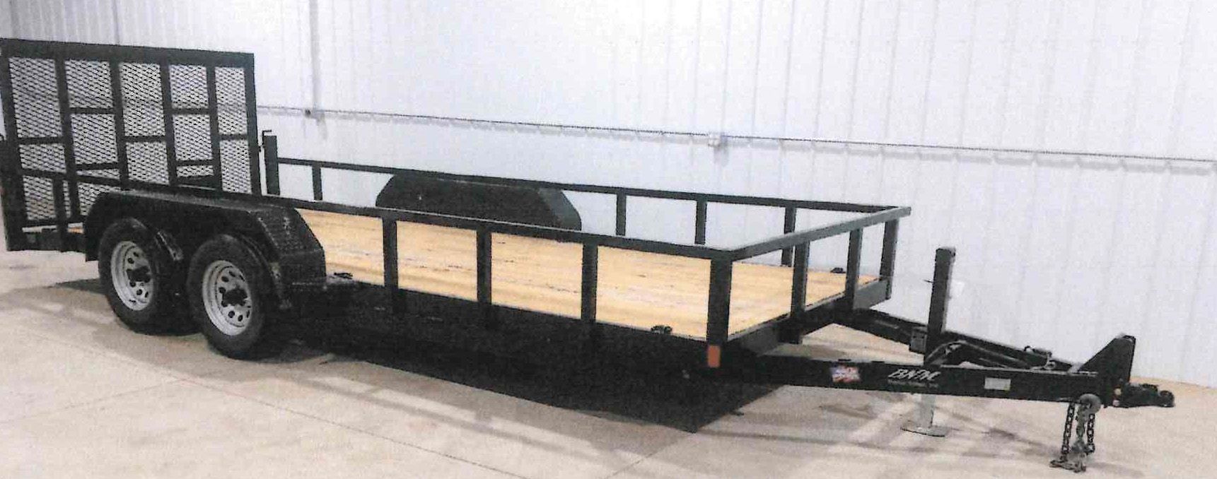 Black utility trailer with metal rail sides and dual axles, parked indoors on a concrete floor.