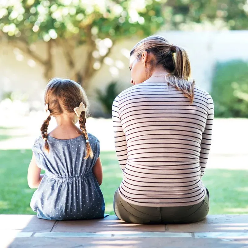 A woman and a little girl are sitting on a bench talking to each other