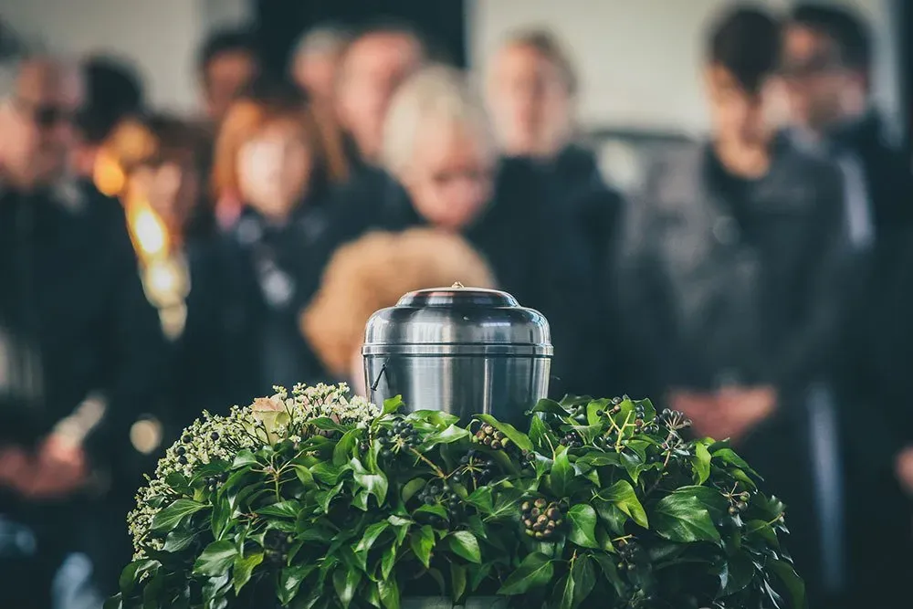 A group of people standing around a urn at a funeral.