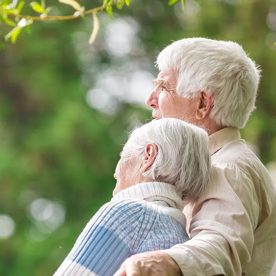 An elderly couple is hugging each other in a park.