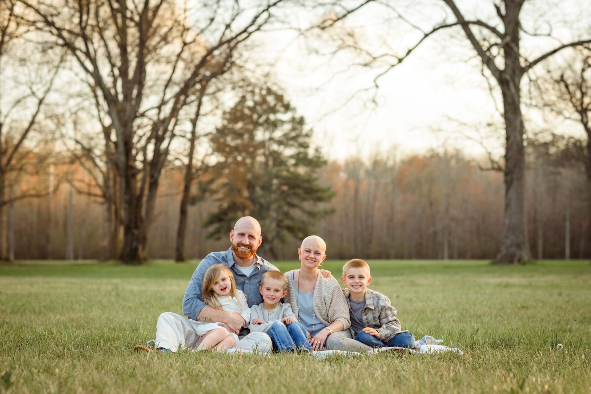 A family is sitting on a blanket in a field.