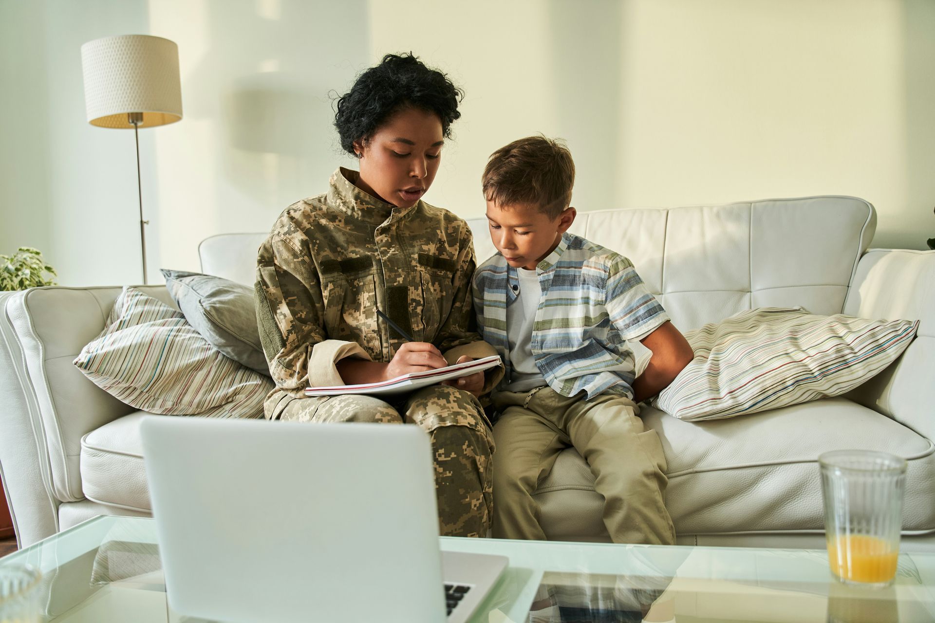 A woman in a military uniform is sitting on a couch with a boy and looking at a laptop.