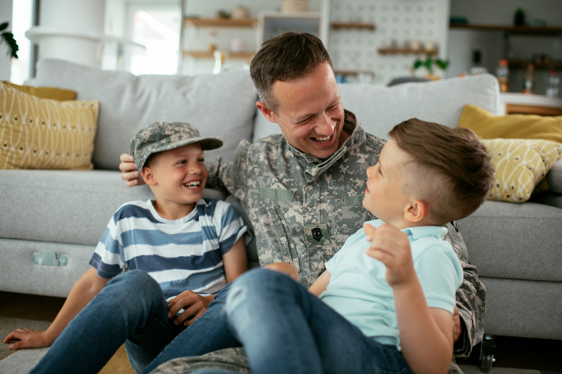 A man in a military uniform is sitting on the floor with two boys.