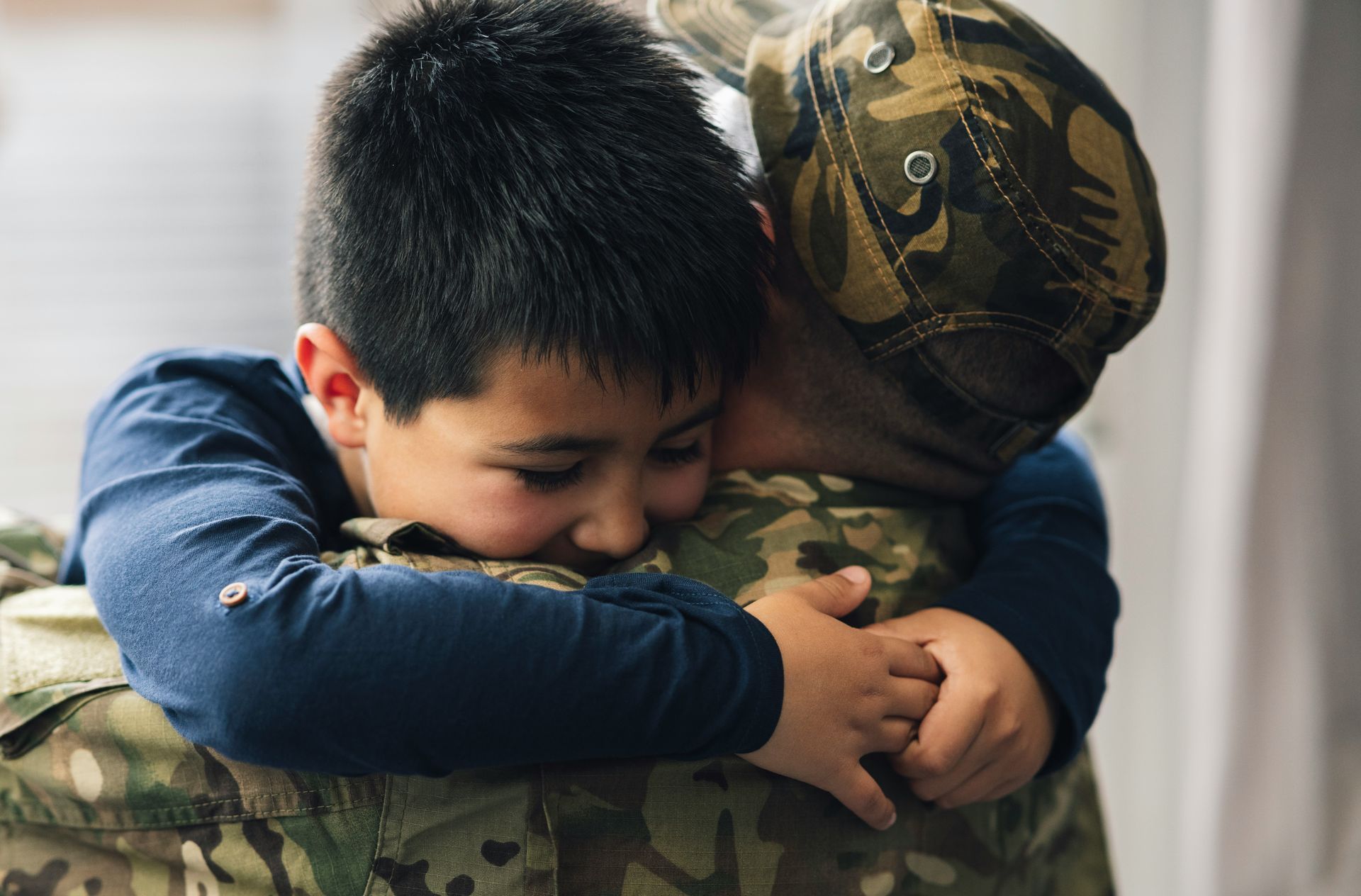 A man in a military uniform is hugging a young boy.