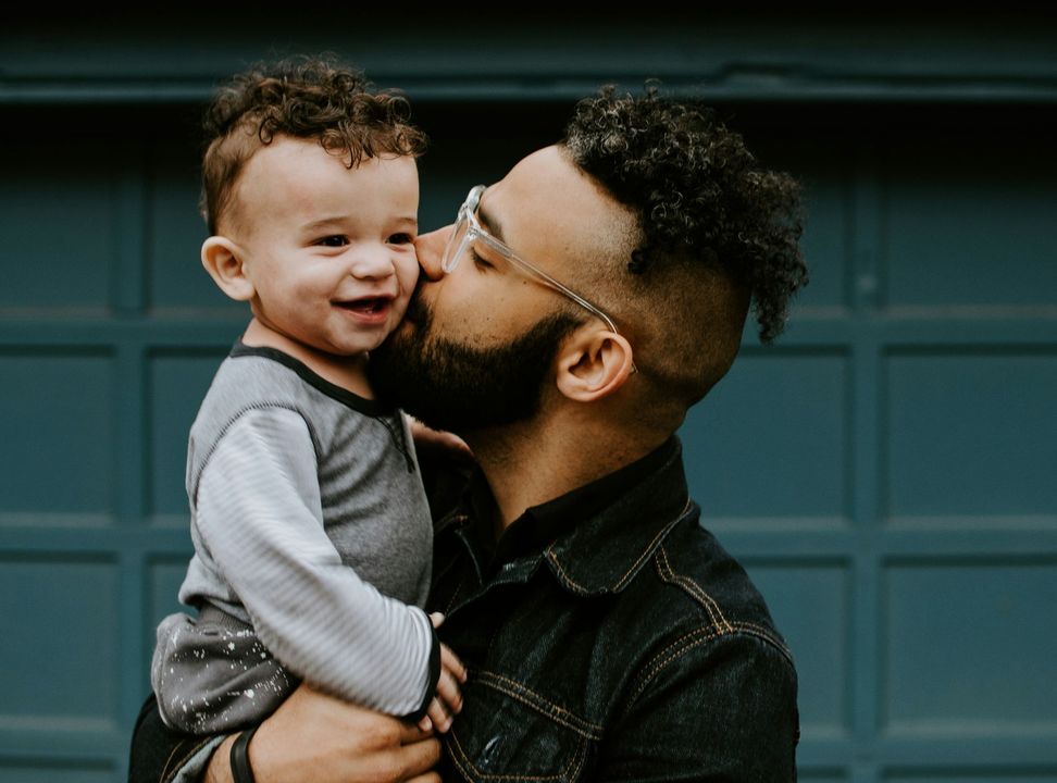A man is holding a baby in his arms and kissing it on the cheek.