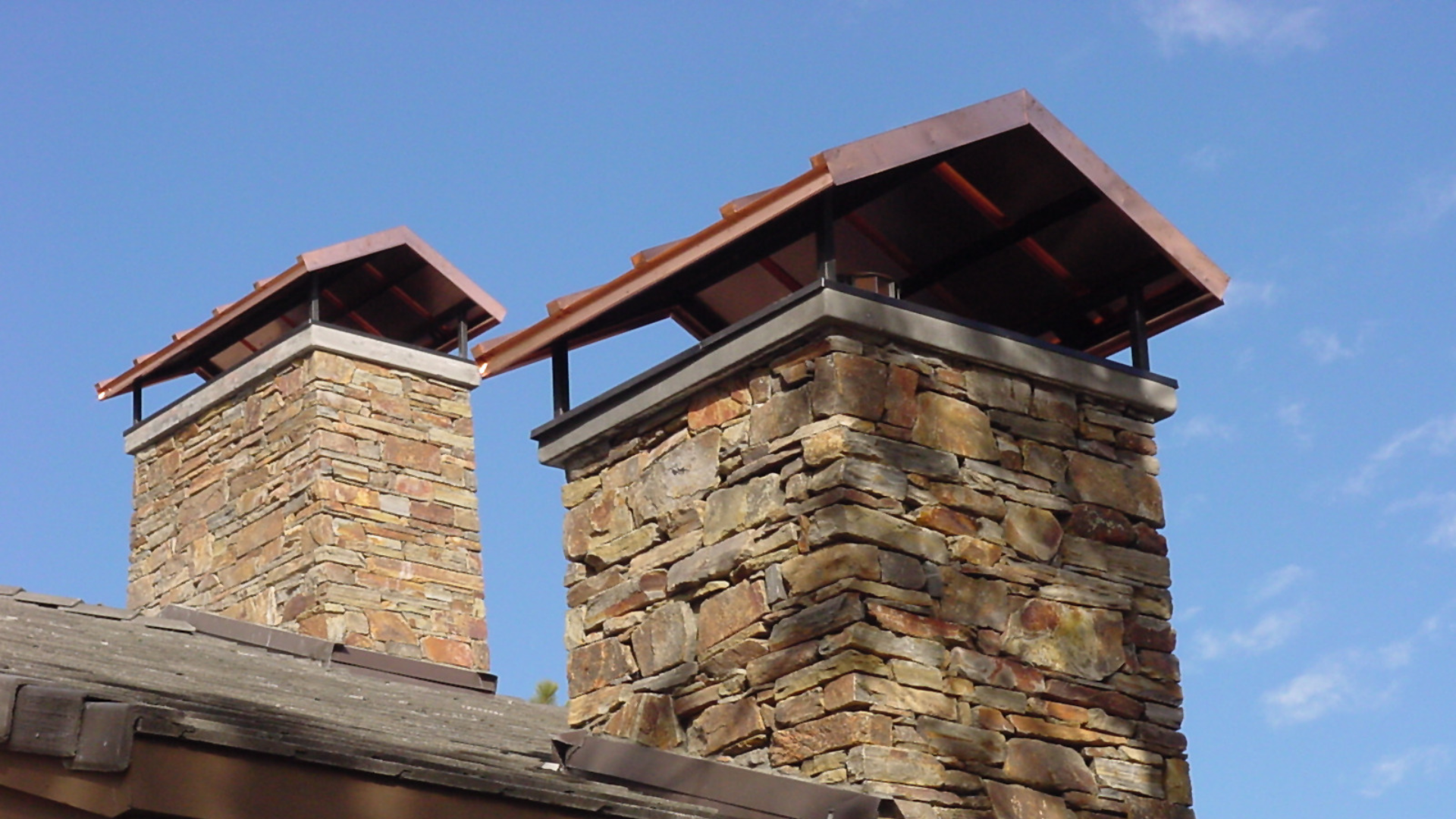 Two stone chimneys with reddish metal caps against a blue sky