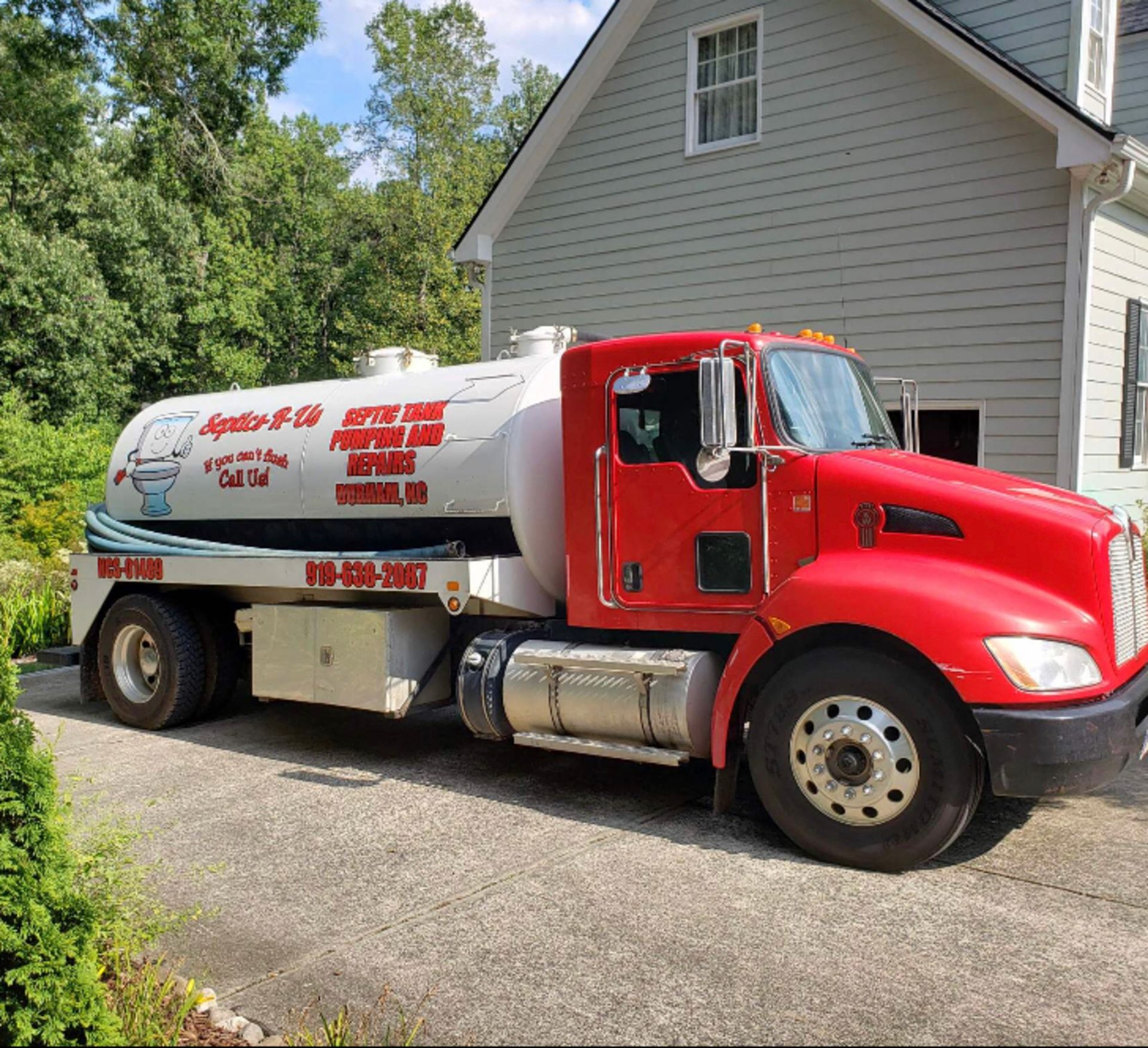 A red septic tank truck is parked in front of a house