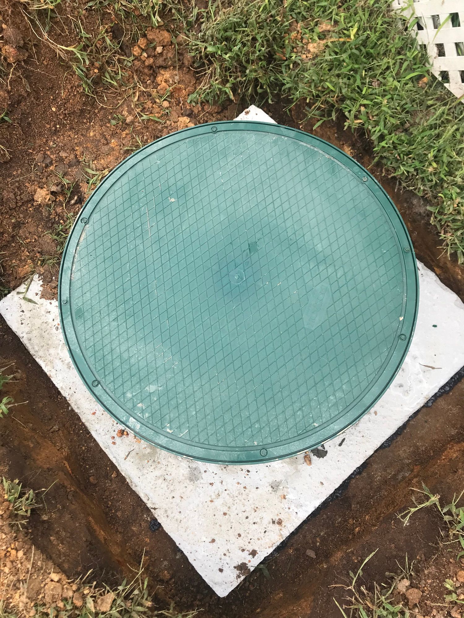 A green manhole cover is sitting on top of a white concrete slab.