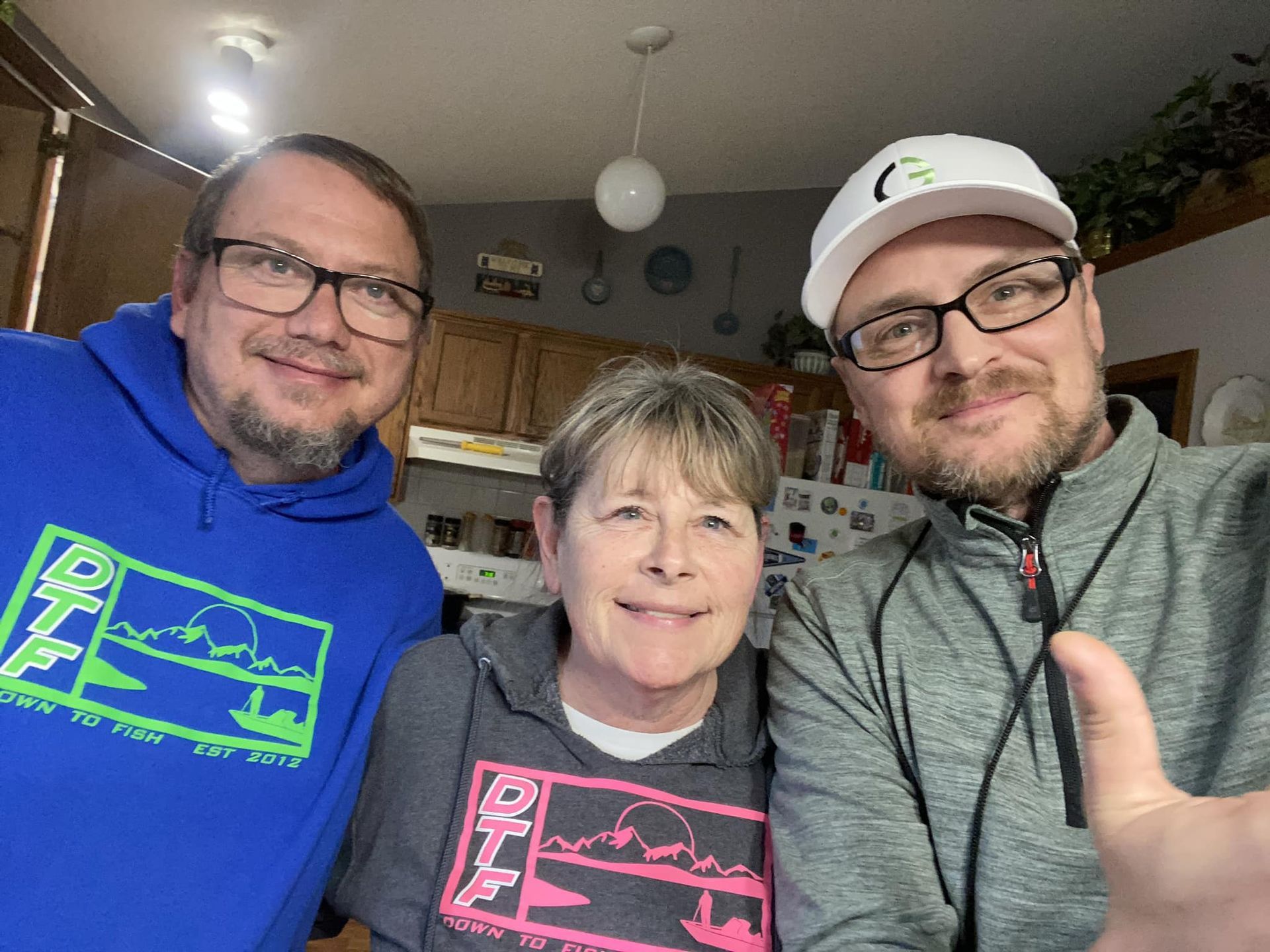 Three people are posing for a picture in a kitchen and one of them is giving a thumbs up.