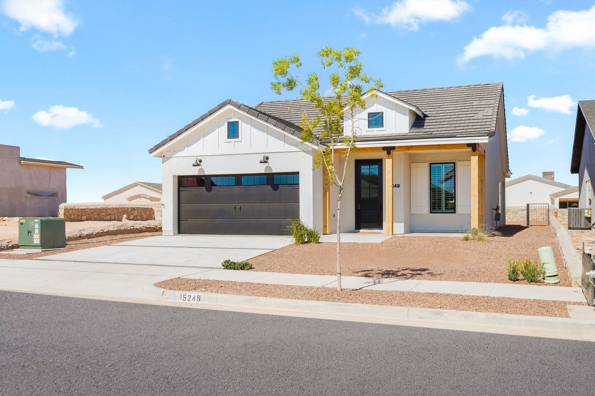 White house with black garage door and wooden accents in a desert setting.