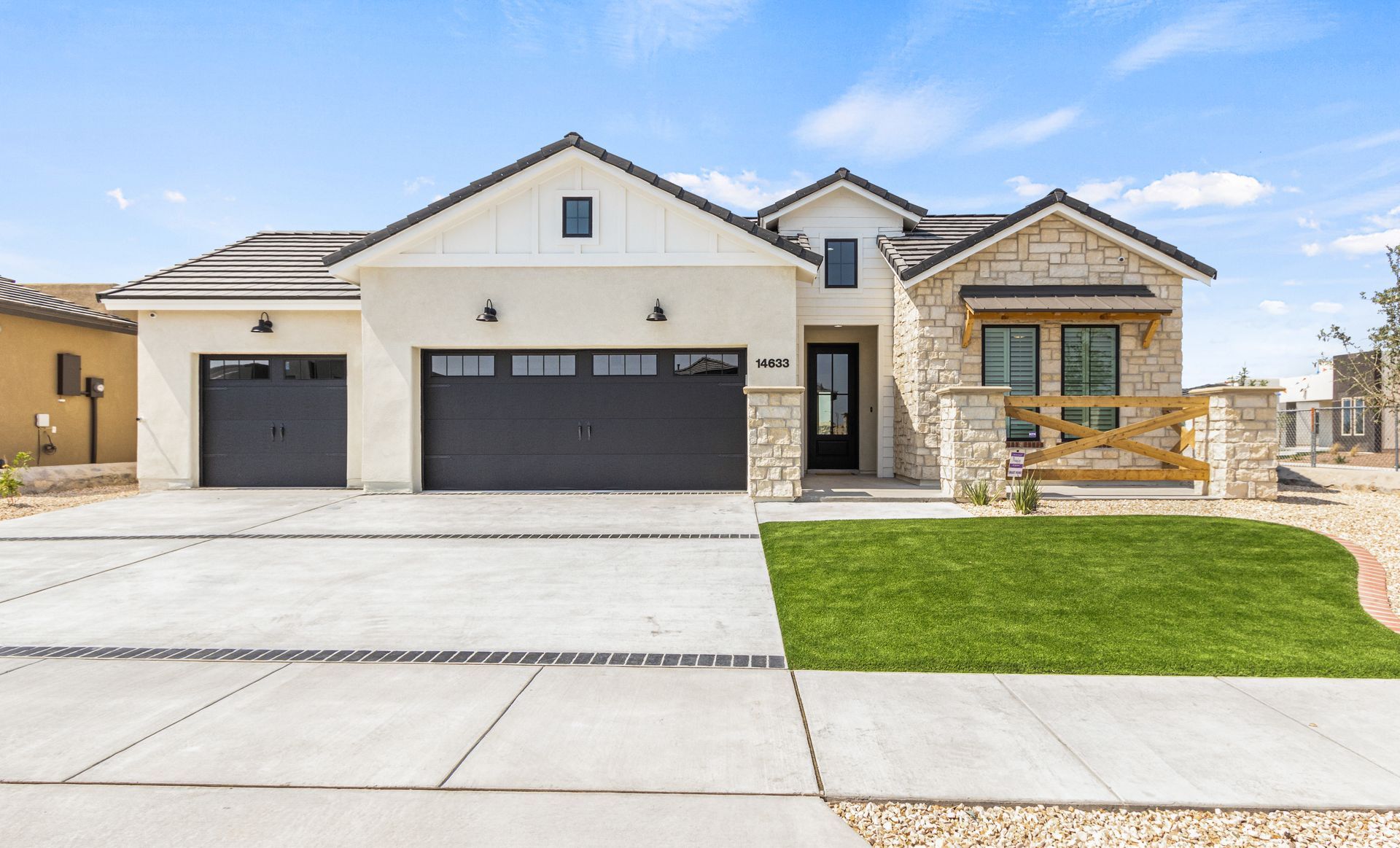 Modern house with stone and white siding, black garage doors, and green lawn.
